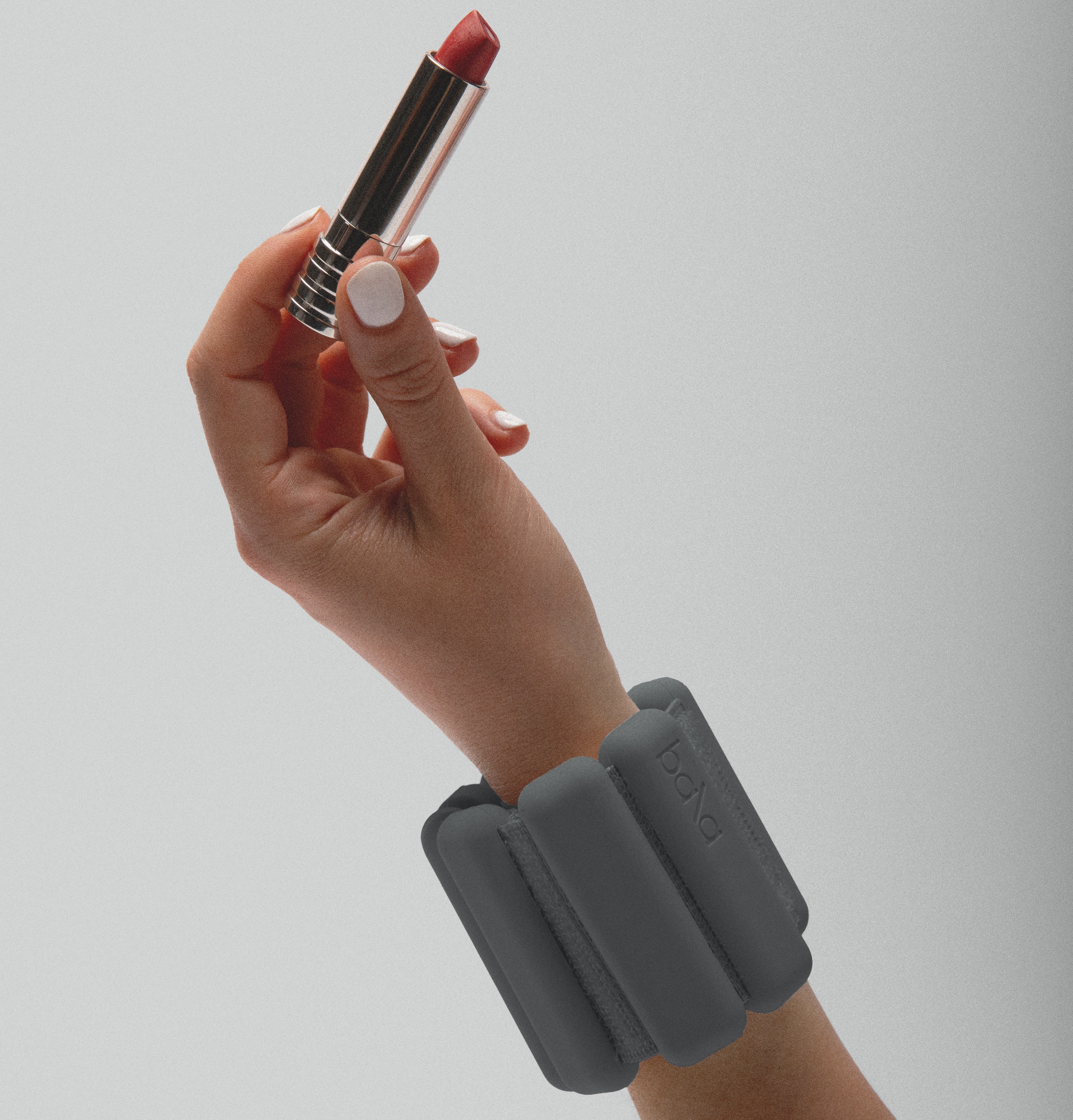 A model’s left hand wearing a Bala bangle in the color charcoal while holding an open lipstick in her fingers.