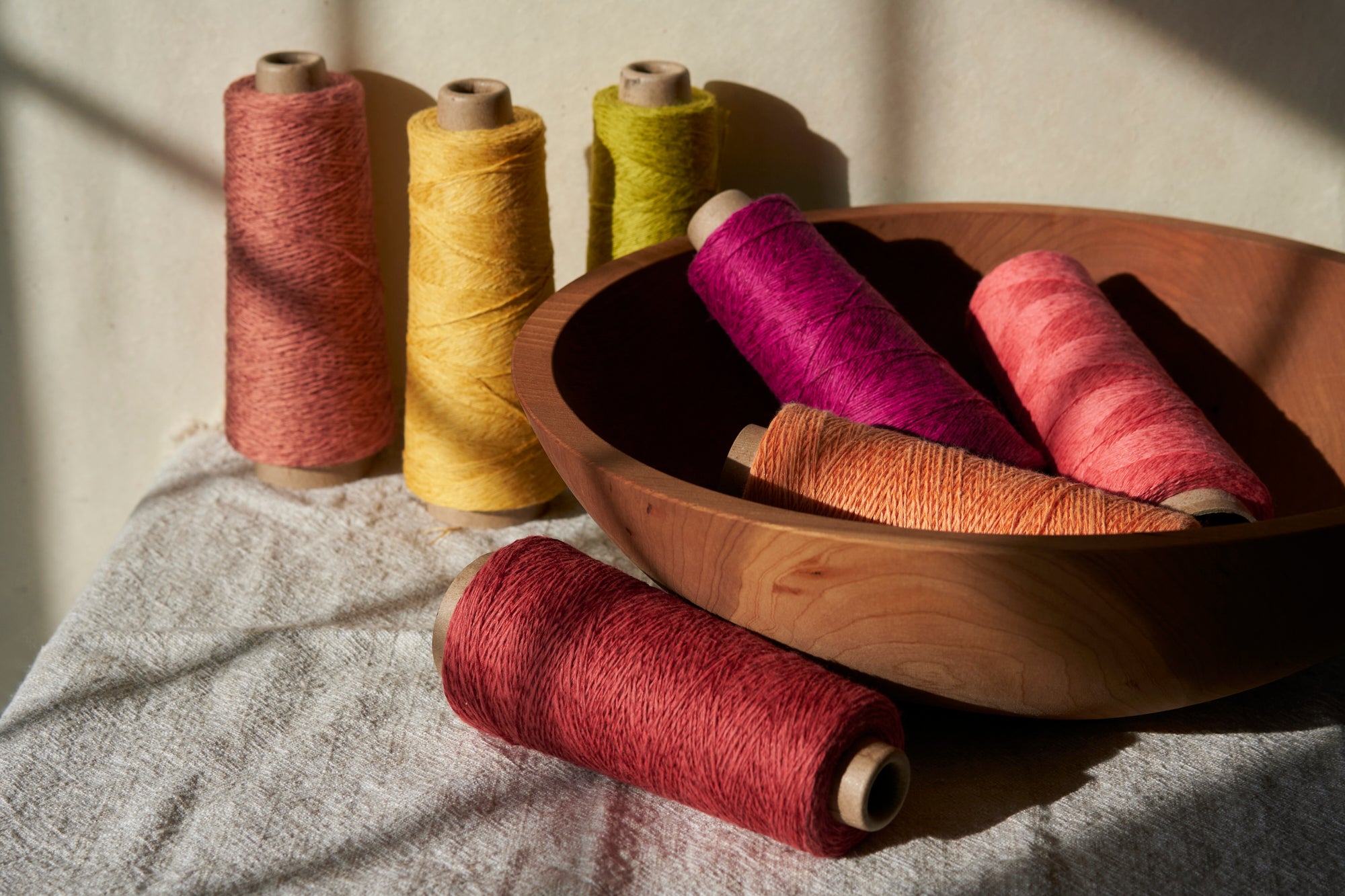 A collection of threads placed in a wooden bowl backdropped by more threads.