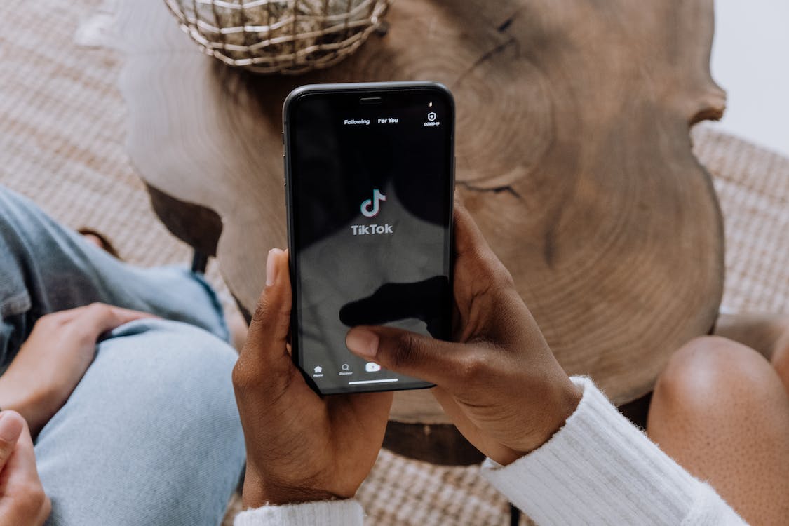 Person holding a smartphone displaying the TikTok app on a wooden table.