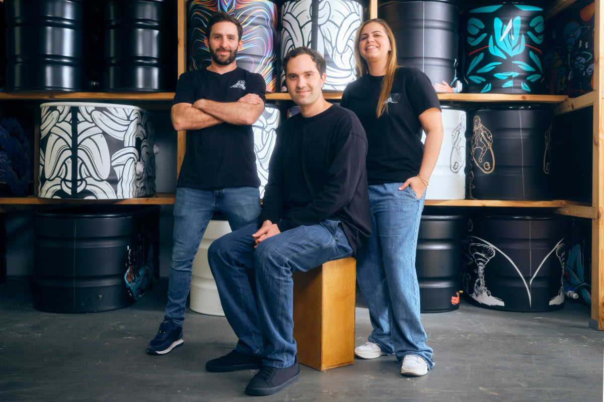 Three Polar Monkeys employees (two men and one woman, all wearing black shirts and blue jeans), are posing in front of a warehouse wall with colorful cold plunges.