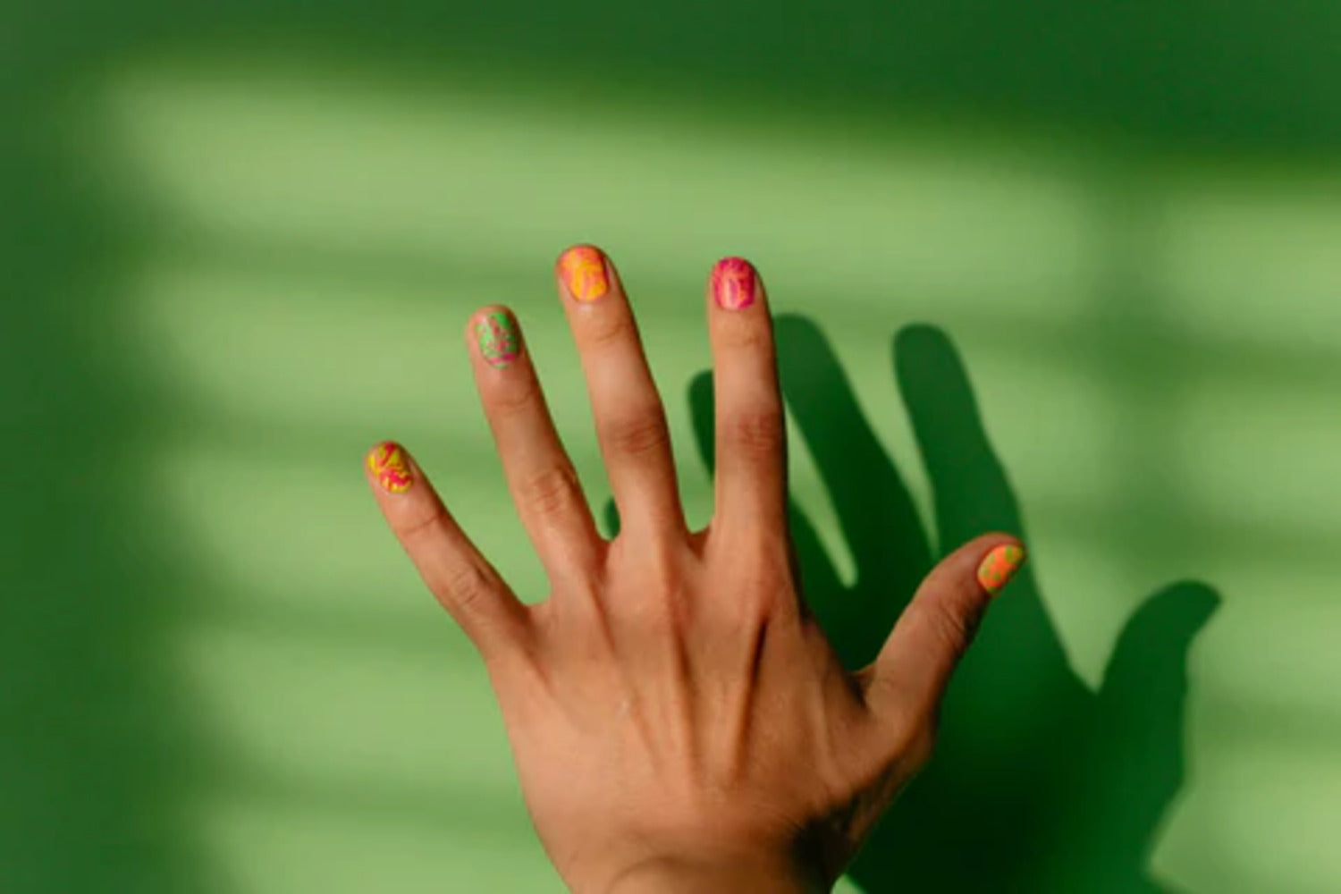 een hand met roze, oranje en groene nagels op een groene achtergrond